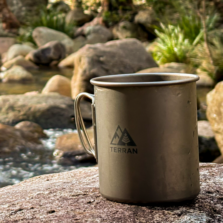 Metal mug with 'Terran' logo on a rock by a stream